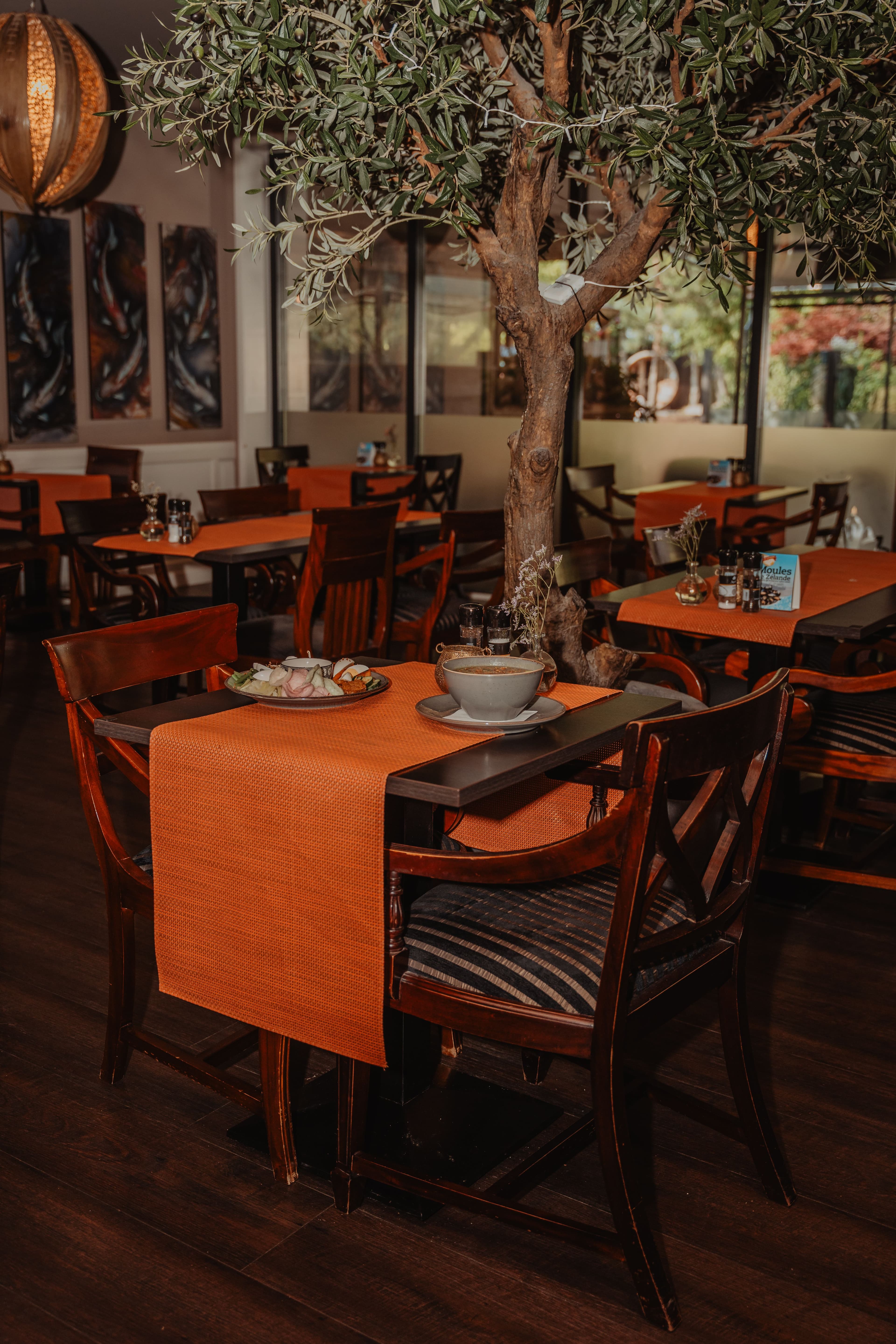 Restaurant met warme houten inrichting en een decoratieve boom in het midden